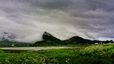 approaching storm over the village by the mountains and lake surrounded by lush meadow. time lapse. lofoten islands, northern norway