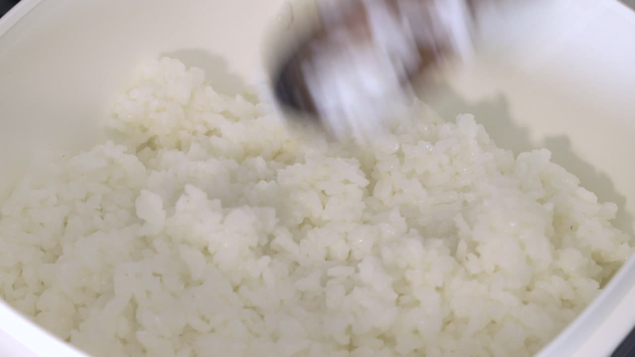 Cooked White Rice Transfer Into A Bowl Using A Wooden Spoon. - close up shot