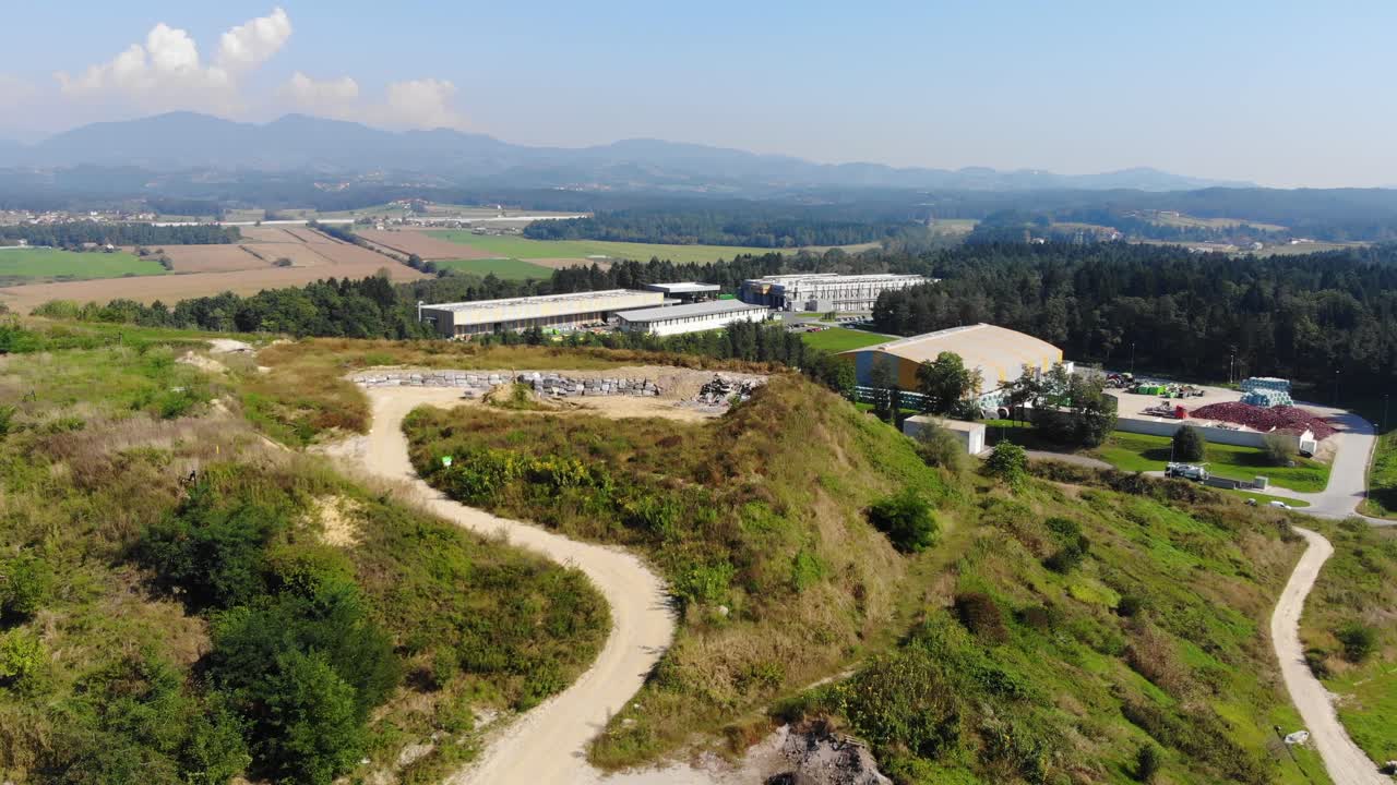 Hill used to store materials for the buildup of industrial waste sites, a plastic recycling plant is seen closeby, Aerial flyover view
