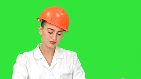 ingeniera estresada con casco comprobando el plan de constricción en una pantalla verde, llave de croma