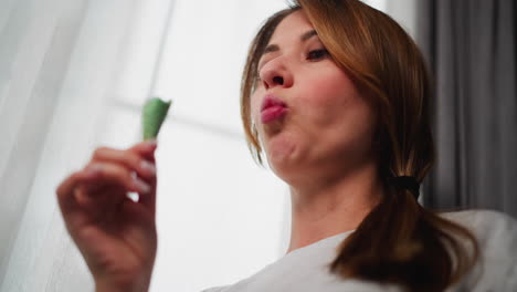 close-up of woman standing by window, eating green ice cream cone. natural light filters through window, creating a relaxed, joyful moment as she enjoys her treat