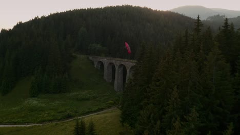 dynamic aerial footage of a paraglider flying over a beautiful old bridge. chmarocsky viaduct in slovakia, central europe.