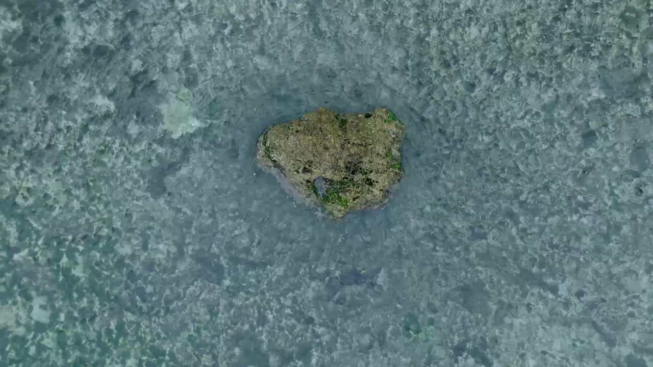 сверху вниз медленный дронный вид волн, разбивающихся над мелким коралловым рифом и большой скалой в улувату, бали, индонезия