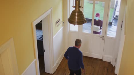 Overhead-view-of-delivery-man-wearing-face-mask-delivering-package-to-senior-man-at-home