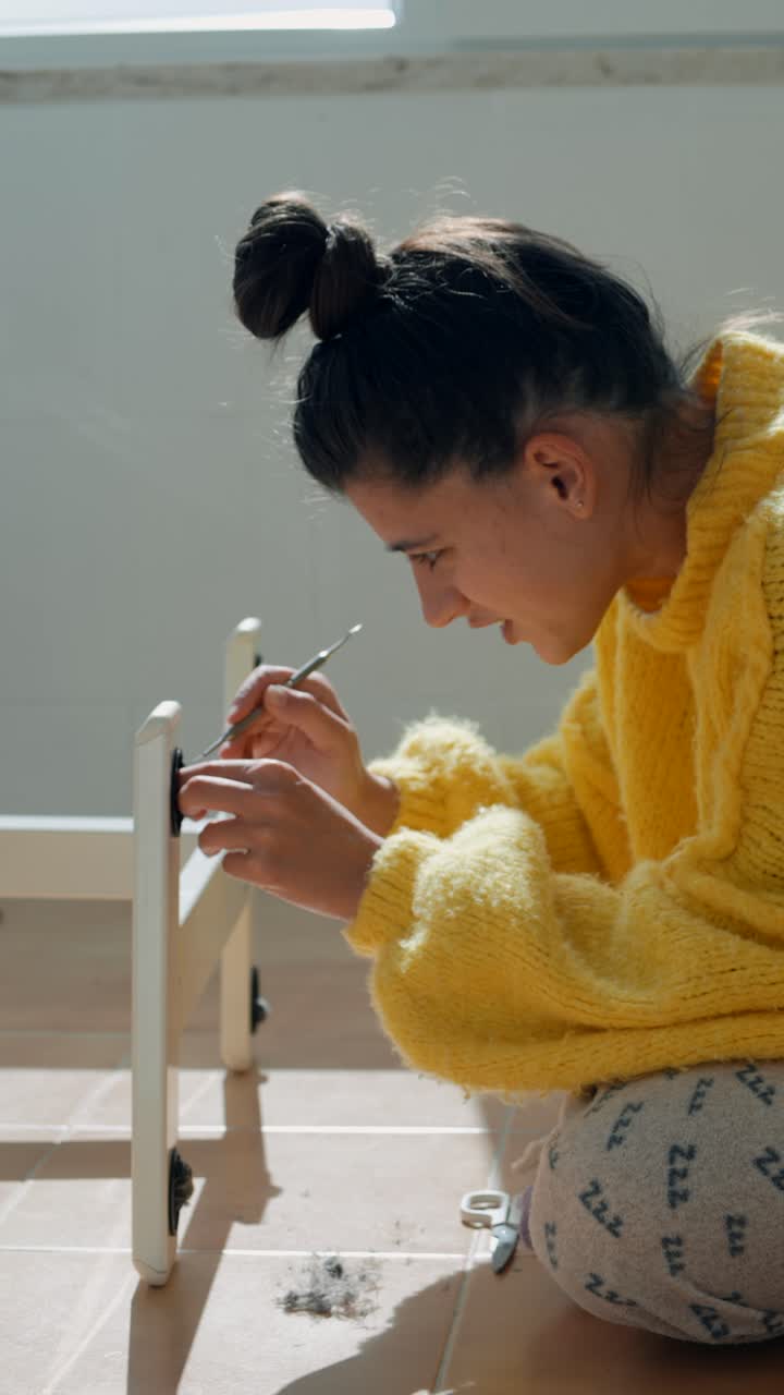 Giovane donna che assembla un piccolo mobile sul pavimento.