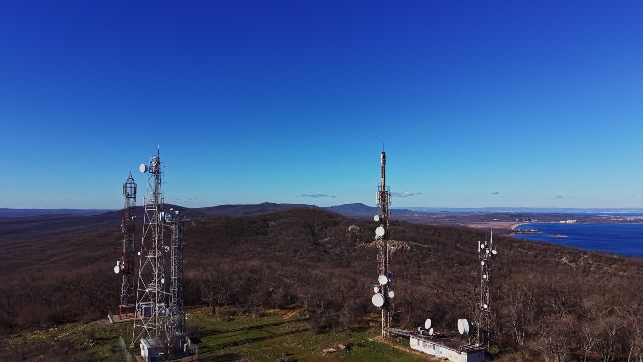 Communication towers stand on a hill near a blue ocean in clear sky