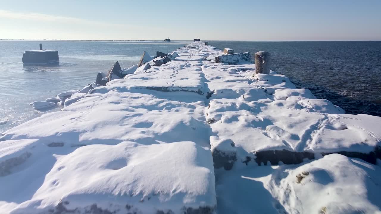 잔잔한 발트해의 눈과 얼음으로 뒤덮인 콘크리트 부두의 공중 전망, 화창한 겨울날 리파자 항구, 저고도 광각 드론이 전진