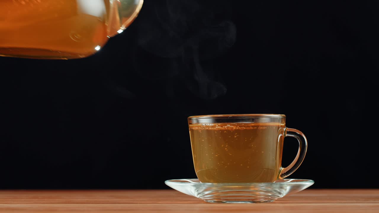 Pouring Hot Tea from a Glass Teapot into a Cup