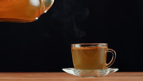 pouring hot tea from a glass teapot into a cup