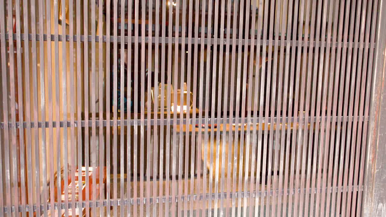 Un'inquadratura statica di una porta a griglia in legno marrone rivela l'interno di un ristorante in penombra.