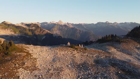 sunset aerial drone shot approaching lone cabin on mount brew peak with rocky mountain landscape in background in canada bc 4k