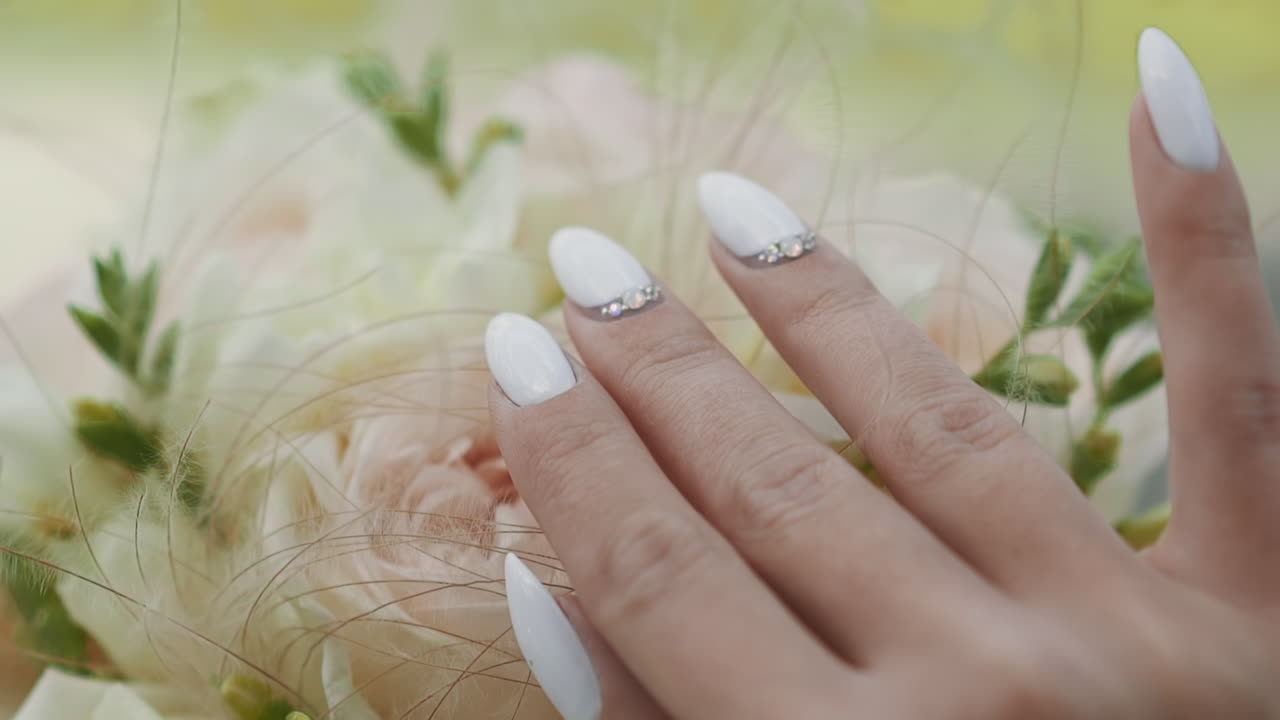 Elegant young bride with white manicure touches bouquet