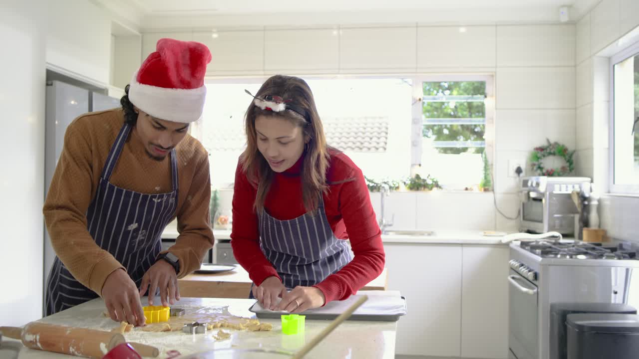 Diverse couple cutting dough with flower and reindeer cutters in home kitchen for holiday baking