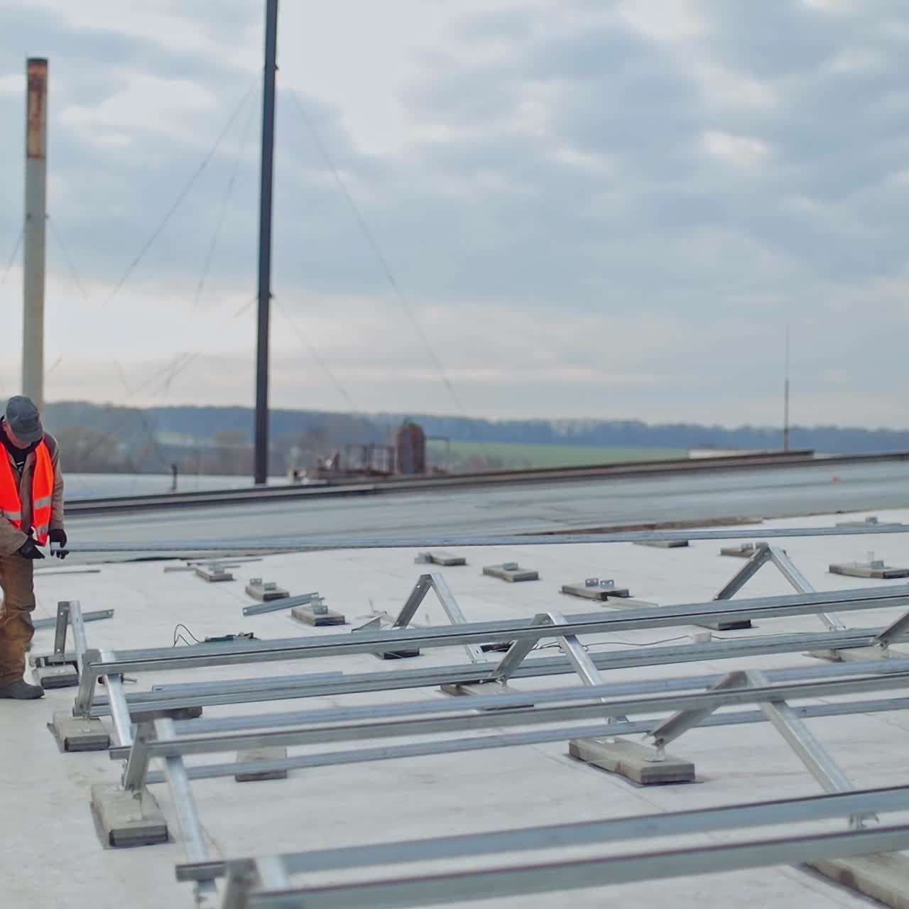 Metal construction on the flat roof of the building. Two workers installing metal base for future solar panels in the new solar power plant.