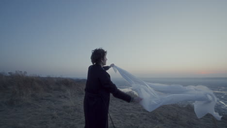 cheerful woman spinning with translucent fabric by frozen lake