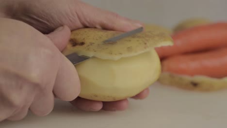 Hands-peeling-potatoes-with-carrots-in-background-close-up