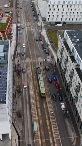 aerial portrait orbiting a tram on the streets of jatkasaari, cloudy helsinki