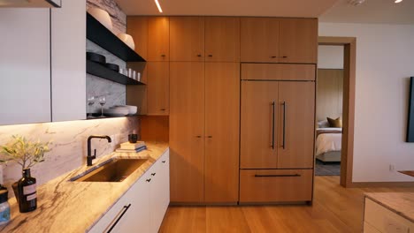 disparo panorámico de una cocina moderna que muestra encimeras y armarios blancos con acabados de color madera claro, creando una atmósfera limpia y acogedora