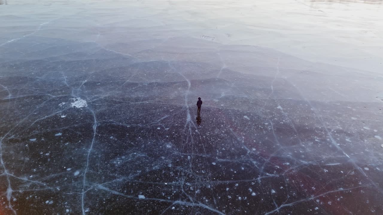 Silhouette of person strolling on ice surface, frozen lake shining with sunset light