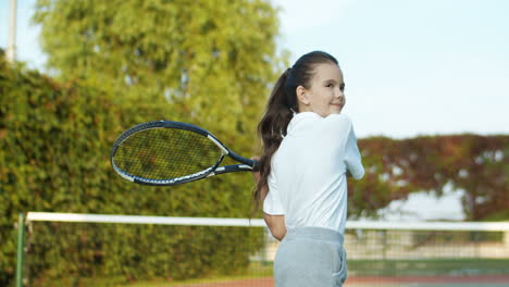 cute little girl training with racket on an outdoor tennis court in summer