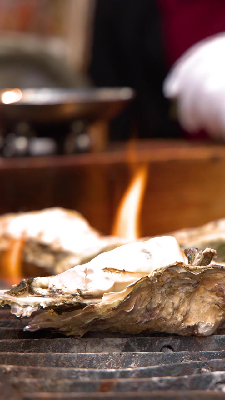 Close-up shot of large oysters cooking on a grill with flames at a Tokyo market.