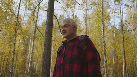 hombre de cabello gris con bigote está paseando por el bosque en el día de otoño disfrutando de la naturaleza y el paisaje explorando la reserva natural