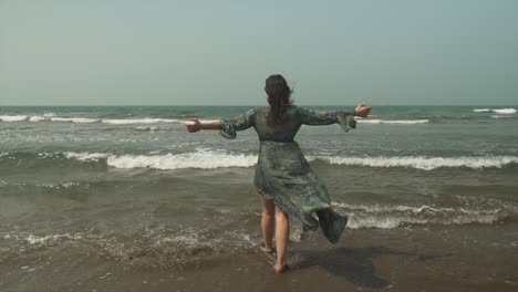 mujer con un vestido de pie en la playa con los brazos anchos hacia el mar