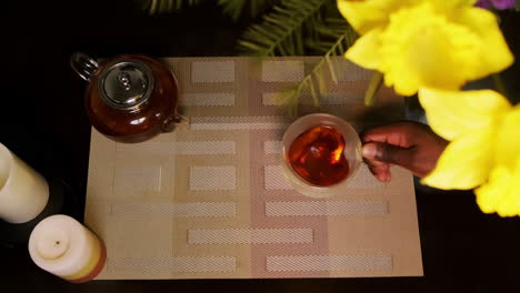 Top-down-shot-of-an-African-American-man-picking-up-a-transparent-heart-shaped-glass-tea-cup-from-a-cozy-dining-table