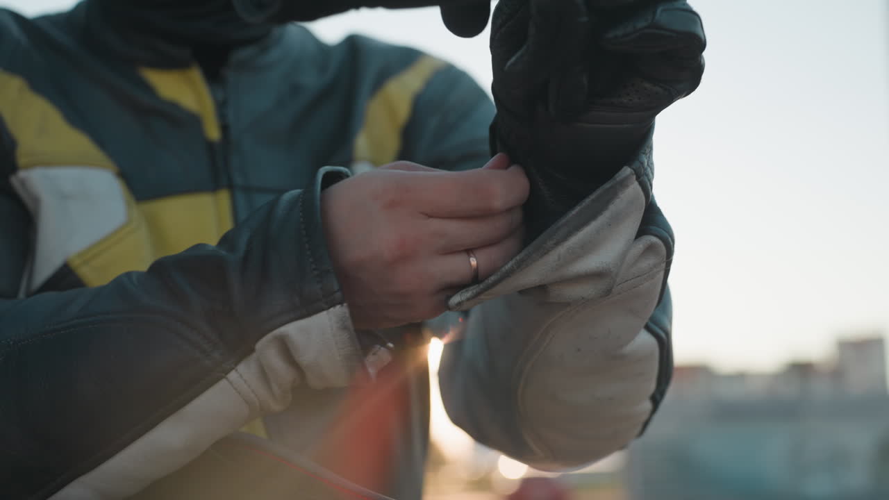 Close up biker preparing for ride putting gloves on under sunlight wearing protective leather jacket showing strength focus and readiness for motorcycle journey