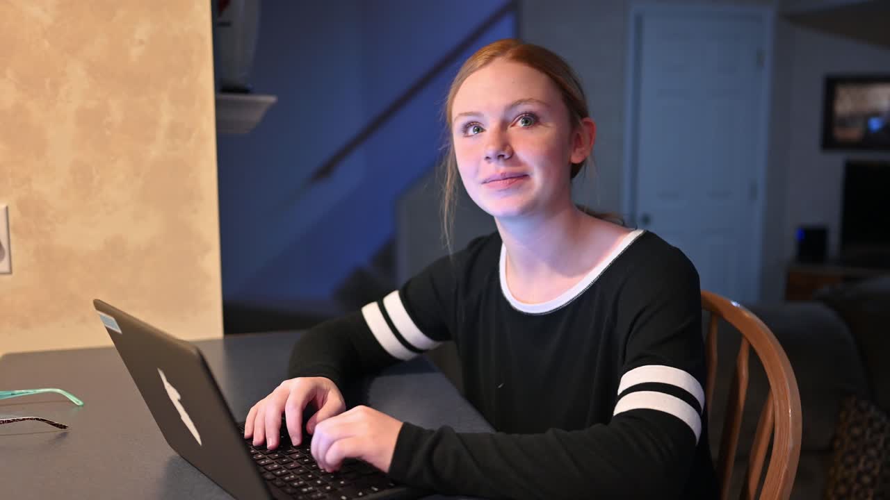 una niña levanta la vista de su computadora, sonríe y sacude la cabeza para estar de acuerdo con el espectador