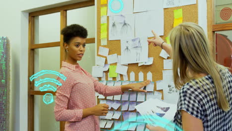 Animation-of-wifi-icons-over-diverse-female-colleagues-discussing-work-in-office