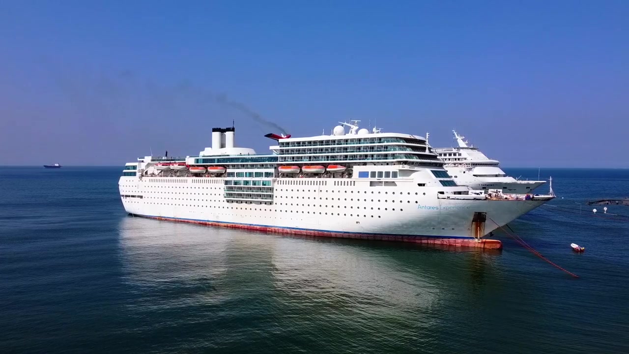 Dramatiske luftoptagelser viser et massivt krydstogtskib, der nærmer sig Gadani Ship Breaking Yard nær Karachi, omgivet af blåt hav, skibsdele og rustent metal under en klar dagslyshimmel