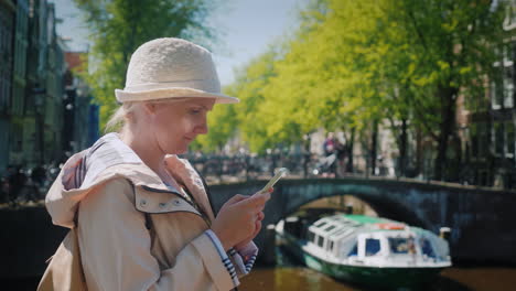 mujer usa un teléfono inteligente cerca del canal de amsterdam