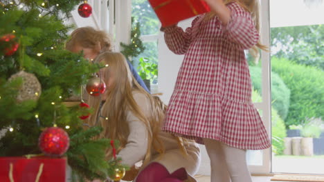 tres niños emocionados corriendo por las escaleras y sacudiendo regalos bajo el árbol de navidad en casa