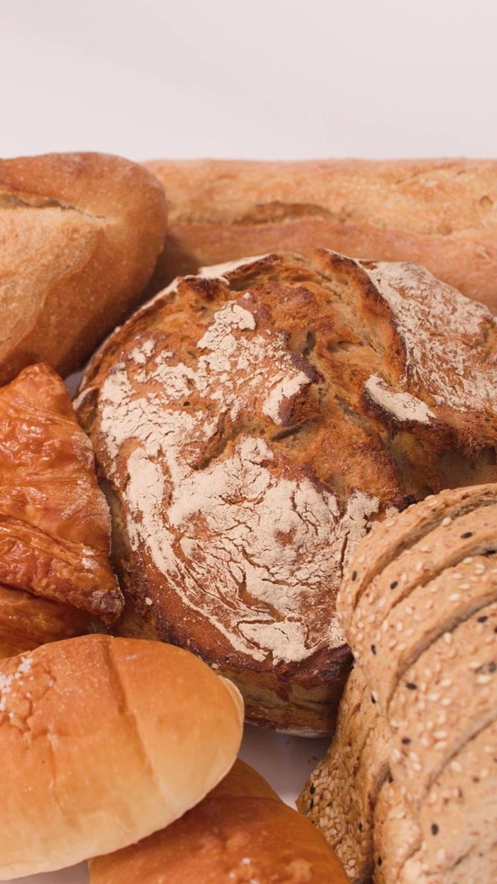 Close-up slow pan across sourdough, baguettes, croissants, and sliced grains under bright studio lighting.