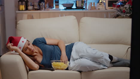 Sleepy-woman-with-santa-hat-watching-television-on-sofa