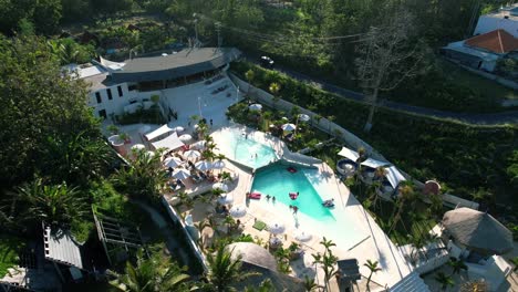 people relax by swimming pool at cactus beach club resort in nusa penida island, indonesia - aerial pull back