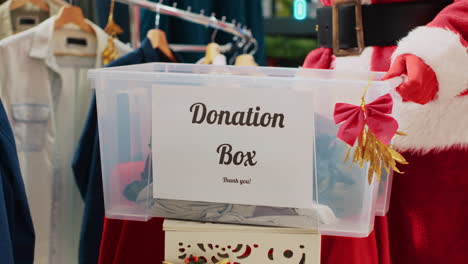 Close-up-shot-of-worker-dressed-as-Santa-Claus-collecting-unneeded-clothes-from-customers-in-donation-box,-giving-them-as-presentduring-Christmas-season-humanitarian-efforts,-spreading-holiday-cheer