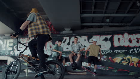 young hipster racing bmx bicycle at skate park with graffiti on wall.