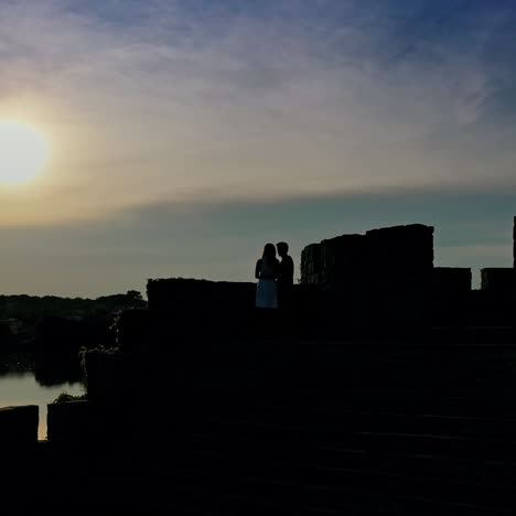 lovely girl and her boyfriend meeting in an old castle near the river at dusk. young beautiful couple standing together in the evening near lake.