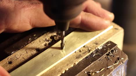 close-up of drill of drilling into brass metal with man's hand and drill shavings spiralling up drill bit