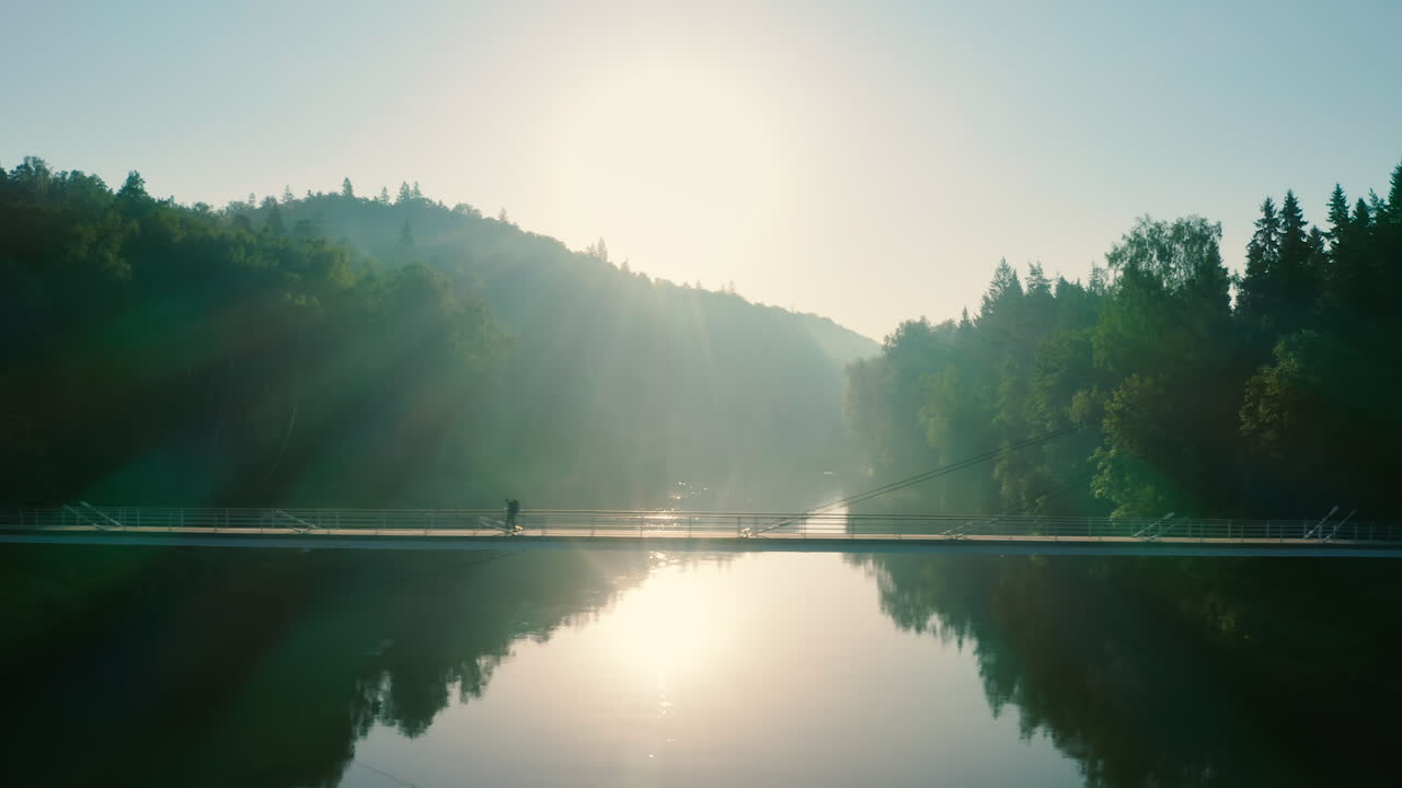 일몰 때 강 위에 현수교를 건너는 등산객, 극적인 공중 촬영