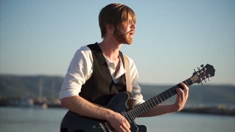 man playing guitar by the water