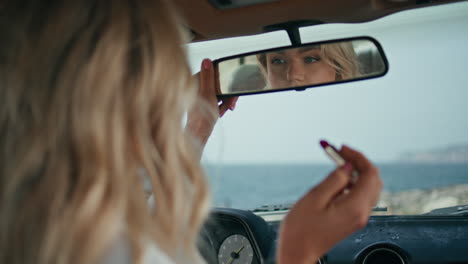 woman applying lipstick in a vintage car