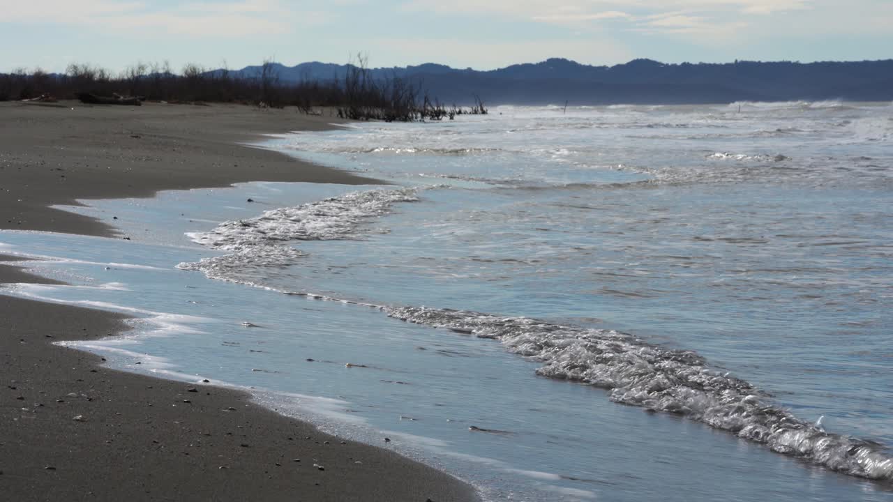 Fredde onde invernali che si infrangono sulla riva sabbiosa umida di un solitario e incontaminato paesaggio di spiaggia adriatica.