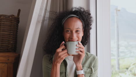 woman enjoying coffee by window, thoughtfully gazing outside, at home, copy space