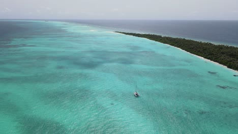 toma de drones del océano índico turquesa con un pequeño yate navegando en aguas tranquilas cerca de la isla tropical maldiva