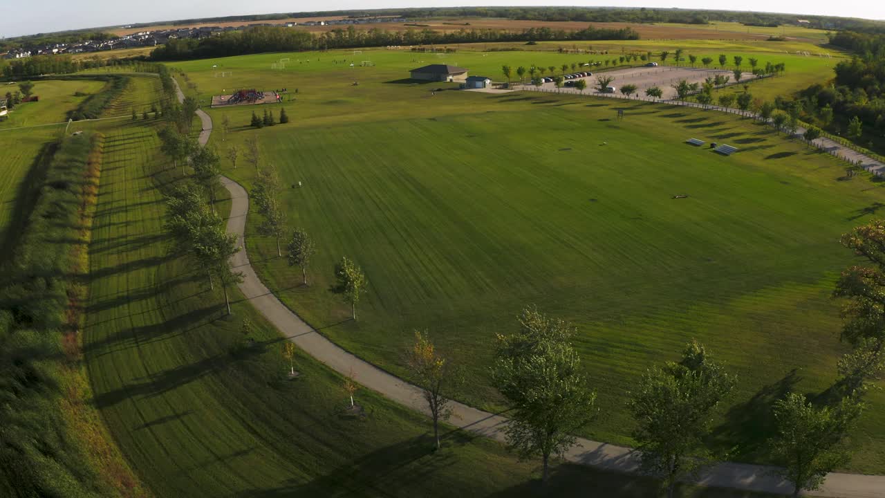 Aerial dolly right of a beautiful lush green soccer park with walking paths and play structures nearby.  Green space.  4k. Golden hour.