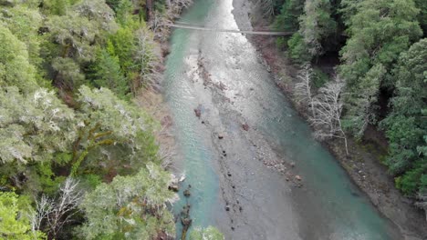 aerial pan up along blue river and suspension bridge in northern california redwoods, usa