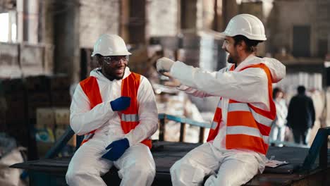 A-man-with-Black-skin-in-a-white-protective-uniform-and-an-orange-vest-plays-rock-paper-scissors-with-a-man-and-loses-to-him-during-his-fun-and-break-at-work-at-a-waste-recycling-and-sorting-plant